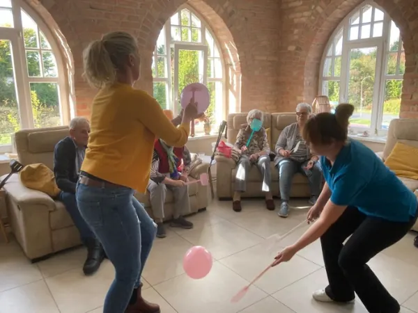 Eine Mitarbeiterin spielt mit Gästen im Aufenthaltsraum Ballon-Tennis.