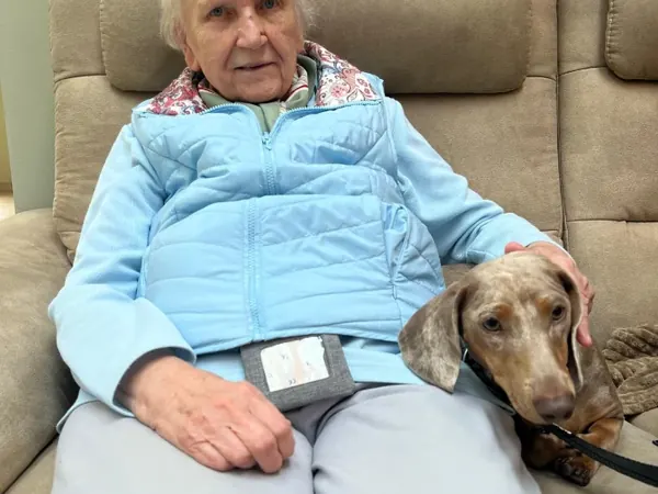 Eine Seniorin ruht im Sessel, neben ihr liegt einer der Dackel.