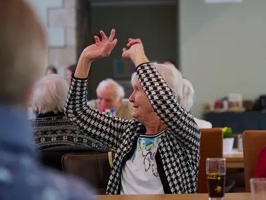 Eine Seniorin bewegt sich mit erhobenen Armen zur Musik.